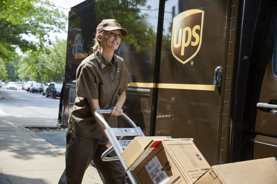 Řidička UPS vykládá zásilky z&nbsp;nákladního vozu pomocí ručního vozíku.
